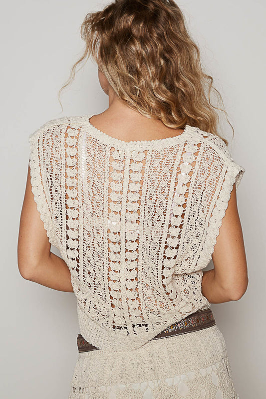 Woman wearing a beige knitted shrug over a dress against a plain background