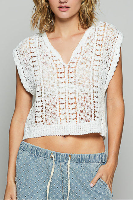 Woman wearing a white crochet top and blue pants against a gray background