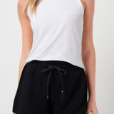 Woman wearing a white sleeveless top and black shorts on a plain background