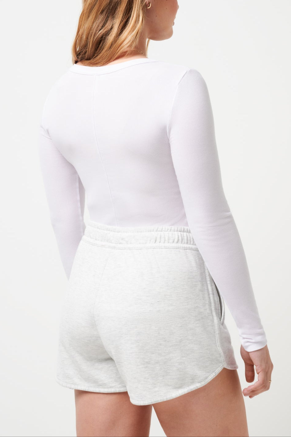 Woman wearing a white long-sleeve top and shorts on a light gray background