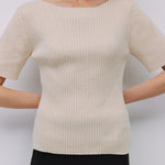 Woman wearing a beige ribbed sweater against a white background
