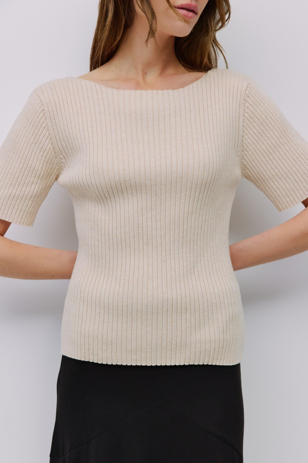 Woman wearing a beige ribbed sweater against a white background