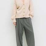 Woman wearing a cream cardigan and gray pants on a white background