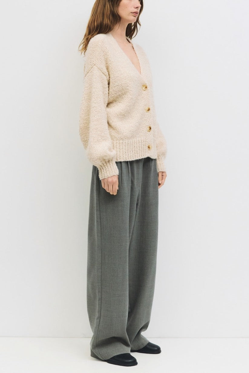 Woman wearing a beige cardigan and gray pants against a white background