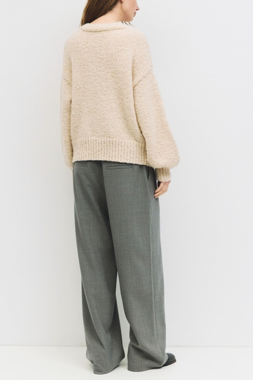 Person wearing a beige sweater and gray pants against a white background