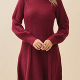 Woman wearing a burgundy knit dress against a beige background