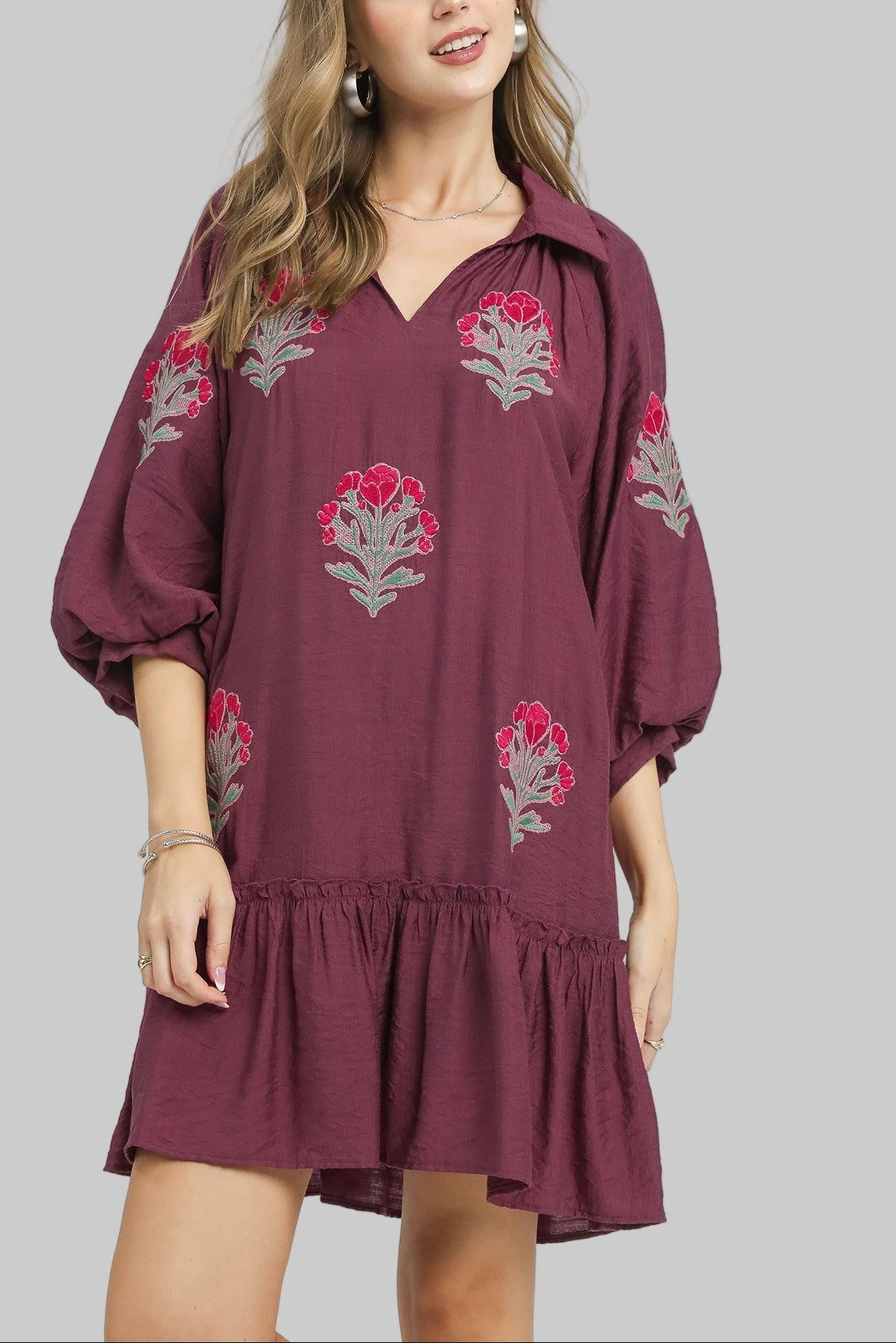 Woman wearing a plum dress with floral embroidery on a white background