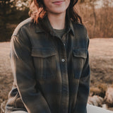 Woman sitting outdoors in a field wearing a green plaid shirt.