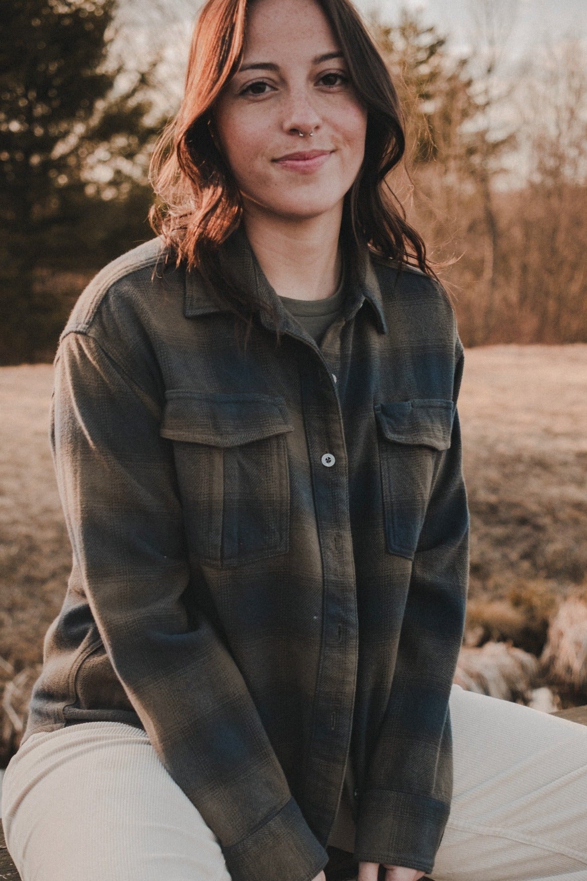 Woman sitting outdoors in a field wearing a green plaid shirt.