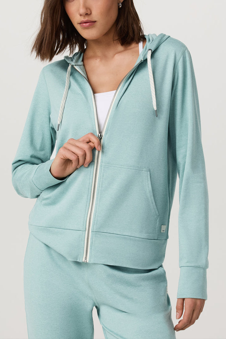 Woman wearing a light blue hoodie and pants on a plain background
