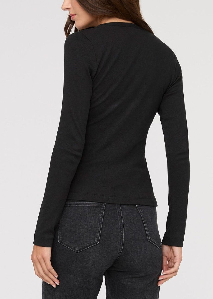 Woman wearing a black long-sleeve top and dark jeans on a light gray background