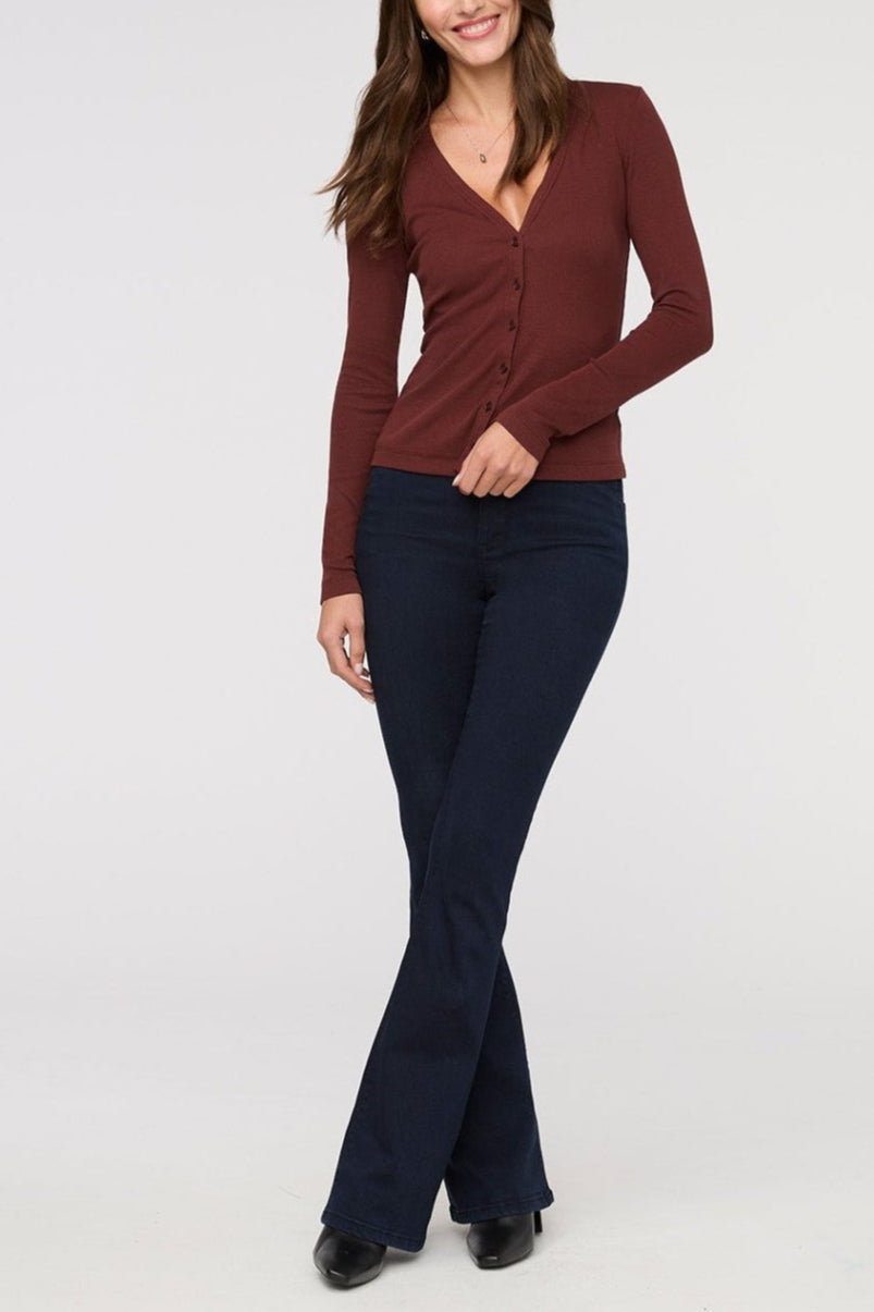 Woman wearing a maroon long-sleeve top and dark blue flared pants on a white background