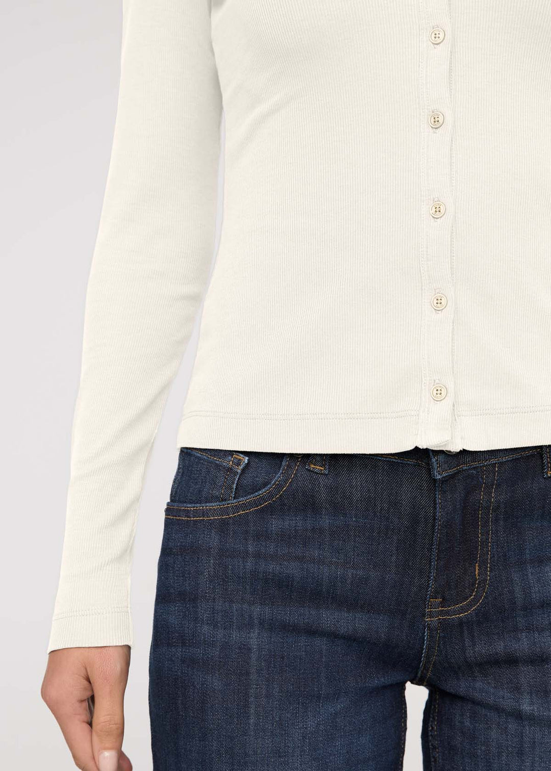 Person wearing a white button-up shirt and dark blue jeans on a light gray background