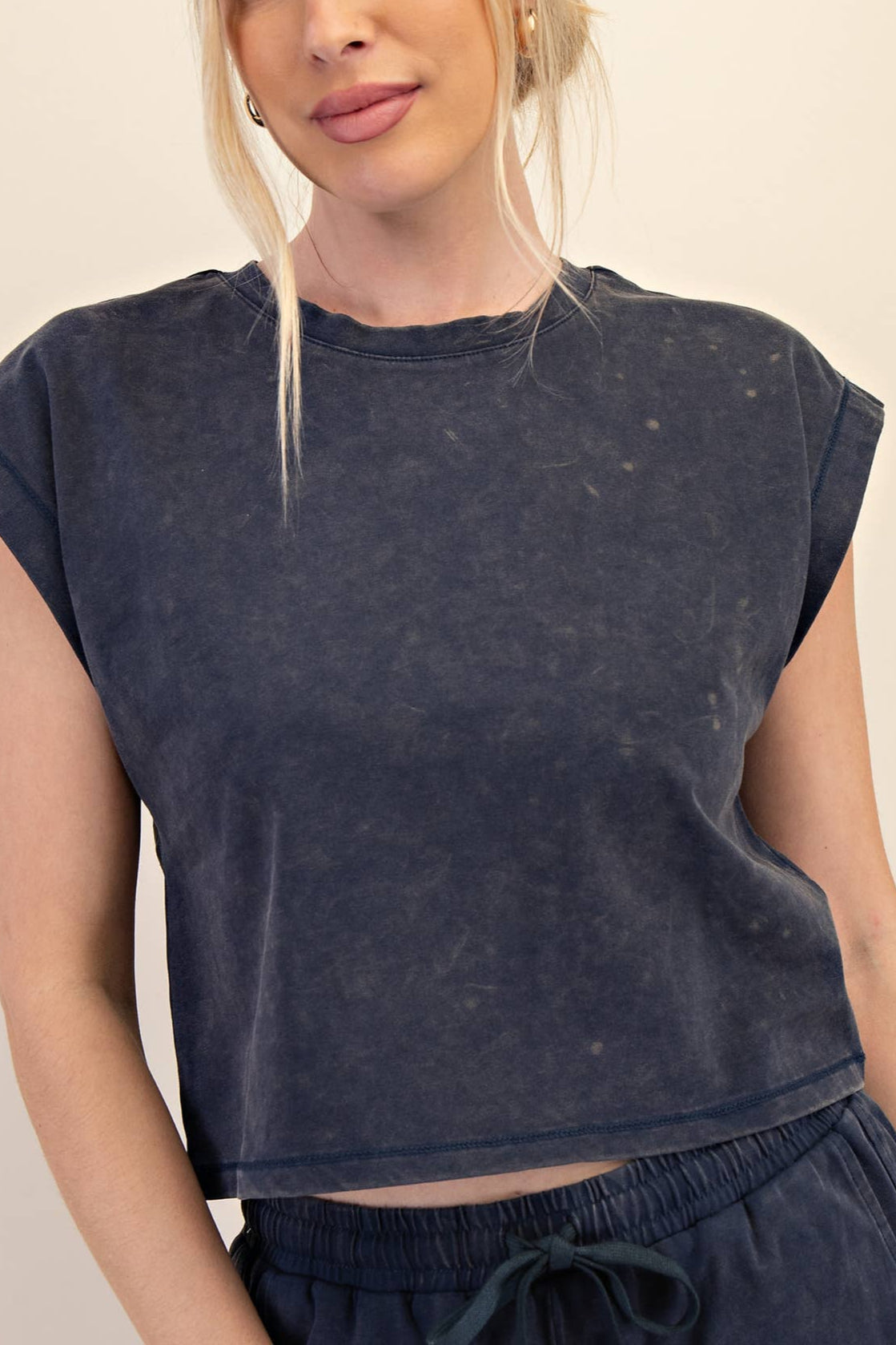 Person wearing a dark blue distressed t-shirt and shorts on a beige background