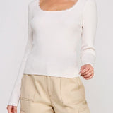 Woman wearing a white long-sleeve top and beige pants on a plain background