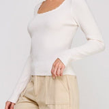 Woman wearing a white long-sleeve top and beige pants on a plain background