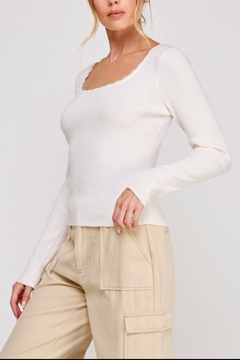 Woman wearing a white long-sleeve top and beige pants on a plain background
