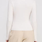 Person wearing a white long-sleeve top and beige pants against a plain background