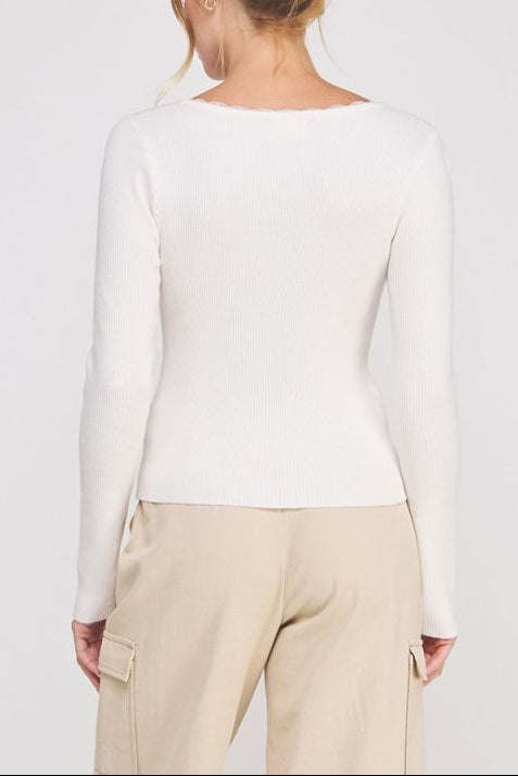 Person wearing a white long-sleeve top and beige pants against a plain background