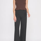 Woman wearing a brown sleeveless top and black pants on a white background
