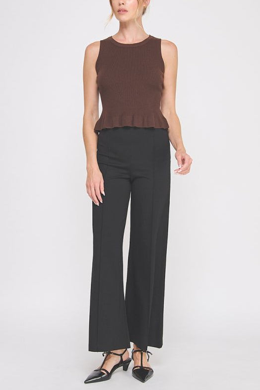 Woman wearing a brown sleeveless top and black pants on a white background