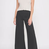 Woman wearing a white sleeveless top and black wide-leg pants on a white background