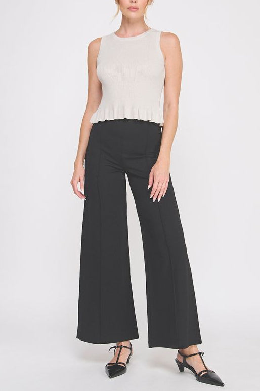 Woman wearing a white sleeveless top and black wide-leg pants on a white background