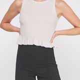 Woman wearing a white sleeveless top with a peplum waist and black pants on a white background