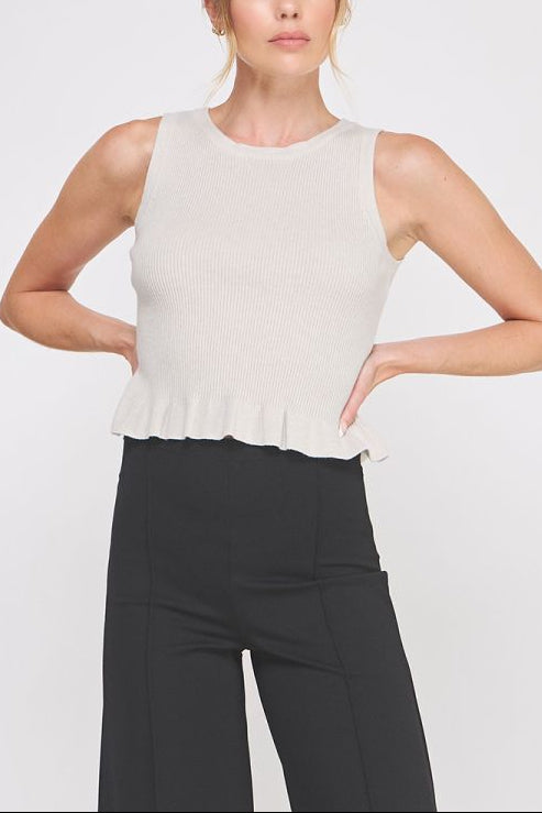 Woman wearing a white sleeveless top with a peplum waist and black pants on a white background