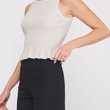 Woman wearing a white sleeveless top with a peplum waist and black pants on a light gray background