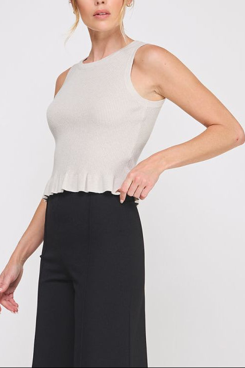 Woman wearing a white sleeveless top with a peplum waist and black pants on a light gray background