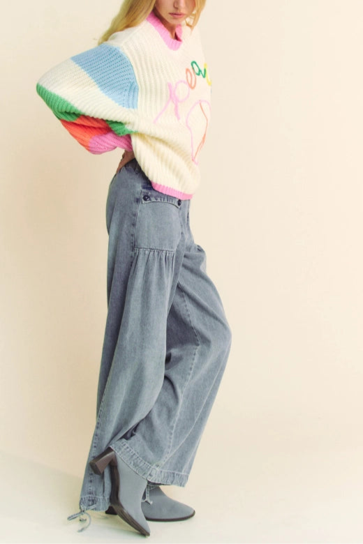 Person wearing a colorful sweater and blue jeans on a plain background