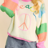 Person wearing a colorful sweater with 'peace' text and design on a beige background