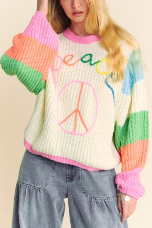 Person wearing a colorful sweater with 'peace' text and design on a beige background