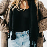 Person wearing a plaid coat, black scarf, black top, and light blue jeans.