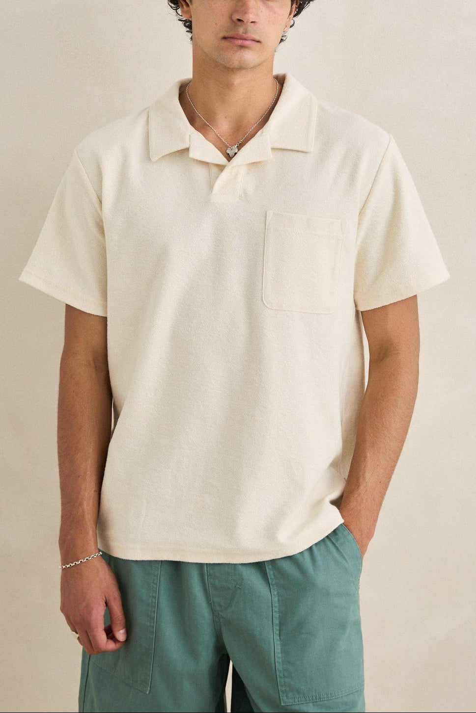 Man wearing a beige polo shirt and green pants against a beige background