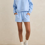 Woman wearing a light blue sweatshirt and shorts set on a beige background