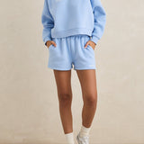 Woman wearing a light blue sweatshirt and shorts set on a beige background