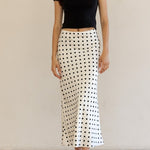 Woman wearing a black top and polka dot skirt against a plain background
