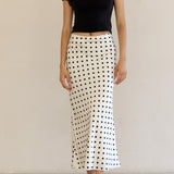 Woman wearing a black top and polka dot skirt against a plain background