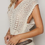 Woman wearing a beige crochet top and skirt with a clutch against a plain background