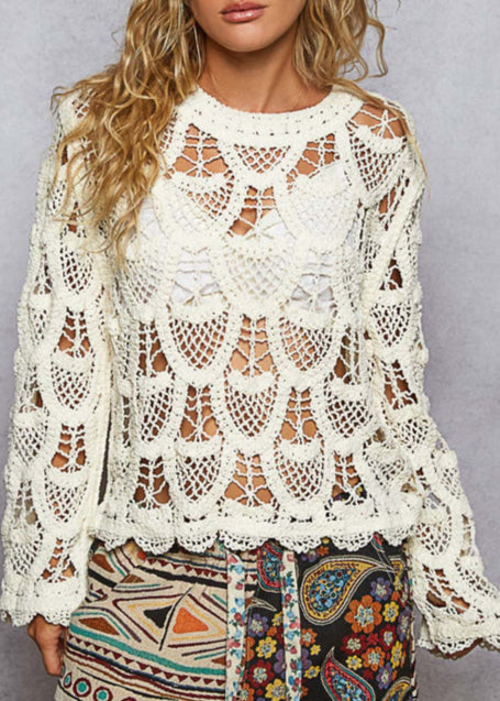 Woman wearing a white lace top with colorful pants against a gray background