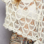 Woman wearing a white crochet top with colorful pants against a gray background