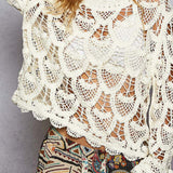 Woman wearing a white crochet top with colorful pants against a gray background