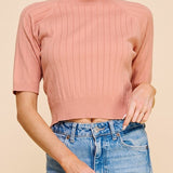 Woman wearing a pink ribbed sweater and blue jeans on a beige background