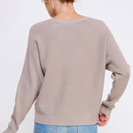 Person wearing a beige sweater and blue jeans on a white background