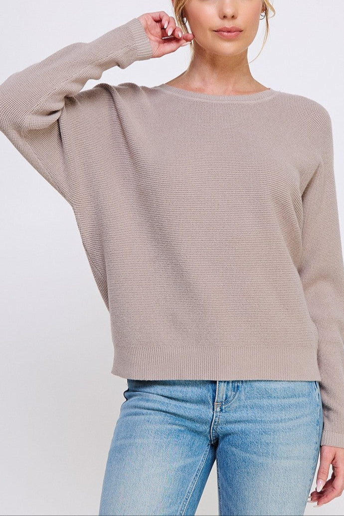 Woman wearing a beige sweater and blue jeans on a white background