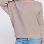 Woman wearing a beige sweater and blue jeans on a white background