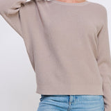 Woman wearing a beige sweater and blue jeans on a white background
