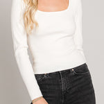 Woman wearing a white long-sleeve top and black jeans against a gray background